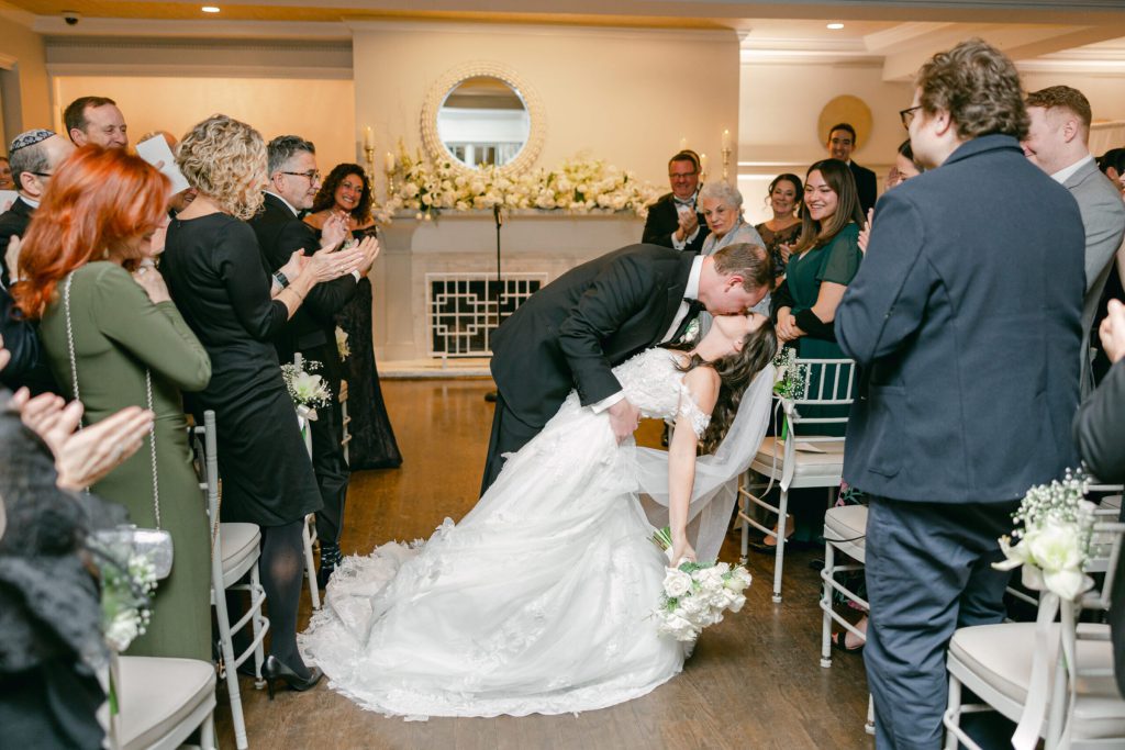 Groom dipping the bride in the aisle as guests applaud.