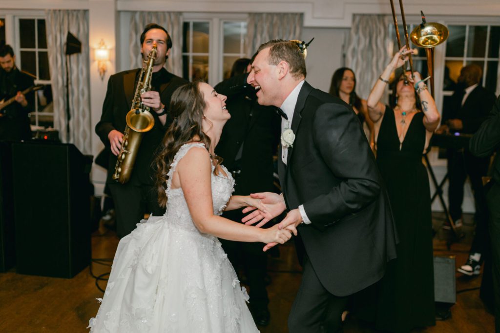 Bride and groom dancing beside a saxophonist and trombonist.