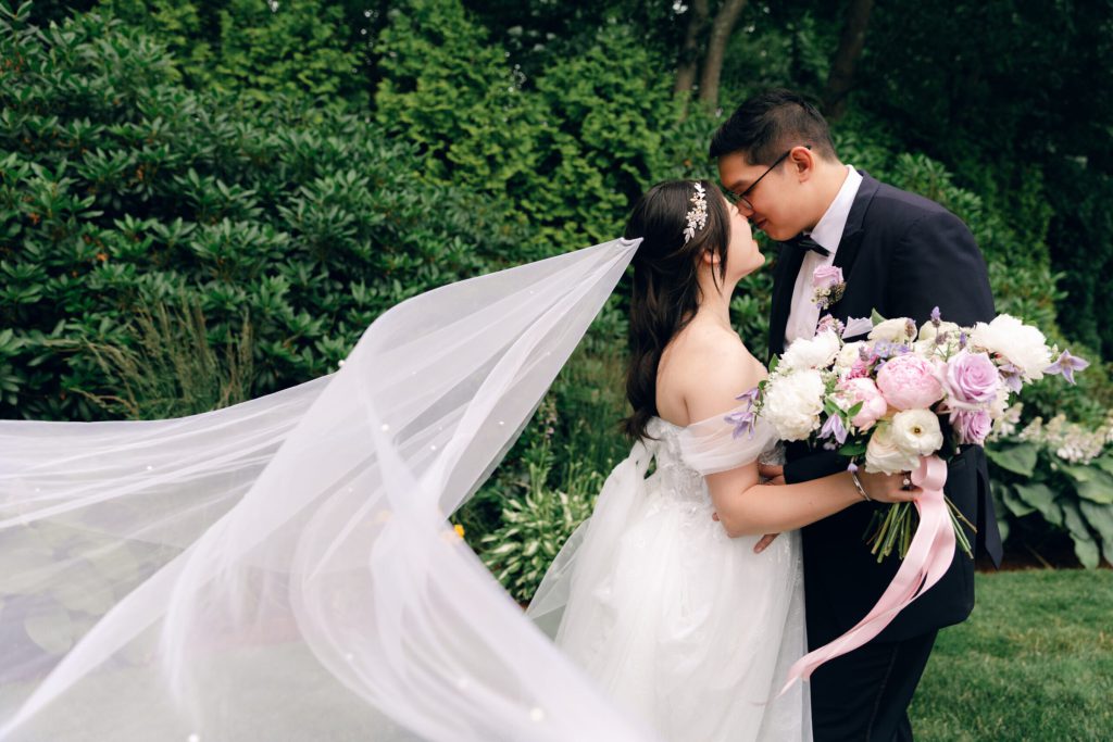 Groom kissing the bride as her veil blows in the wind.