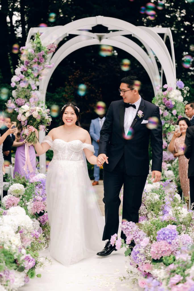 Bride and groom beneath a lavender floral arch during the ceremony.