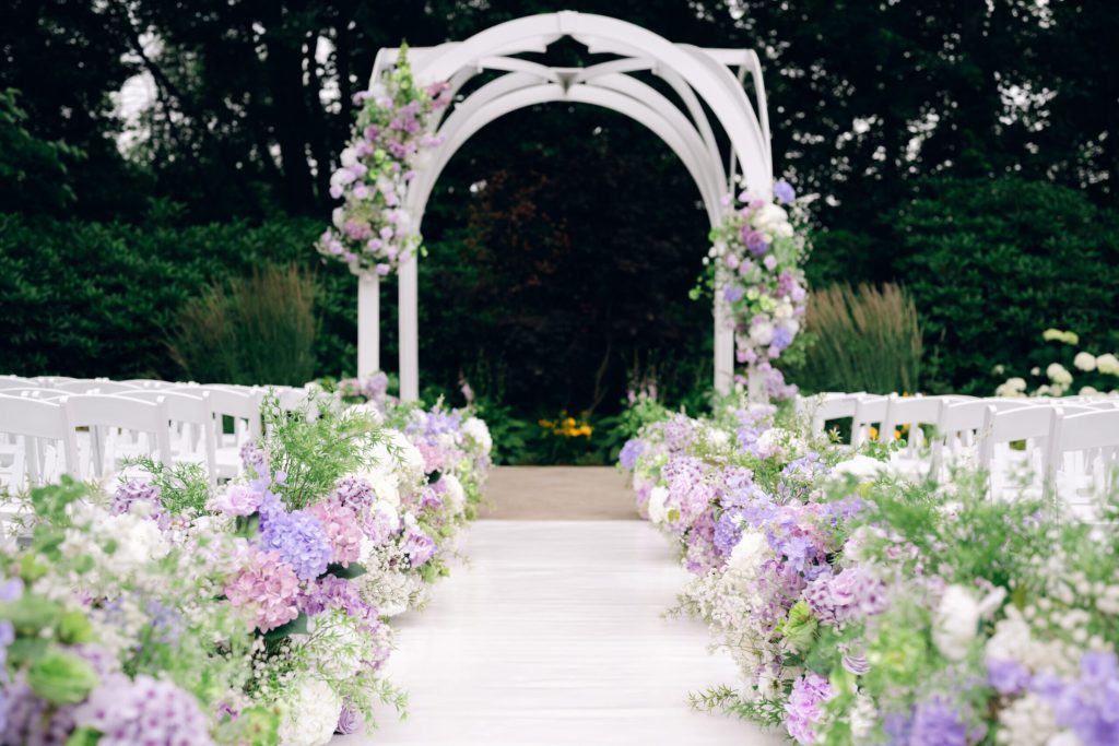 Ceremony aisle lined with lavender and white flowers leading to a white arch.