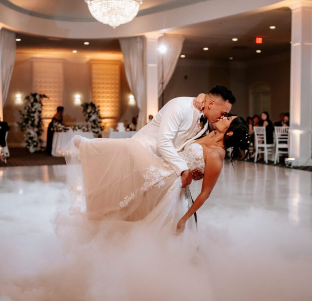 Couple sharing a dip kiss on a fog-covered dance floor in the ballroom at Avenir.
