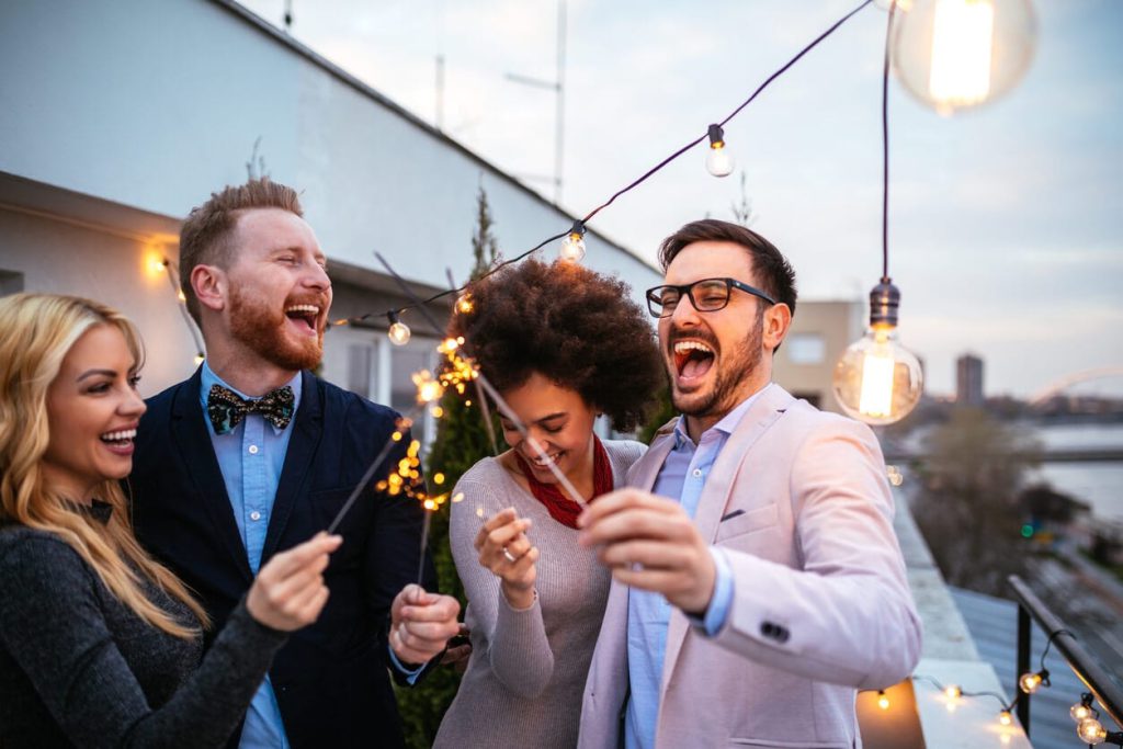 Colleagues laughing with sparklers on a string-lit rooftop